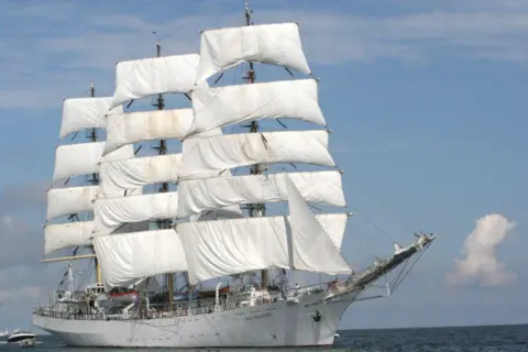 Sail Training International Tall ship - Dar Mlodziezy - with a white hull and white sails, at sea.