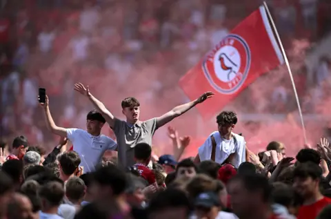 Bristol City fans celebrate on the pitch with smoke flares and flags after clinching a place in the Championship play offs
