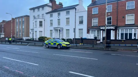 The cordon at the scene in London Road. A police car is pictured in the road next to the cordon. 