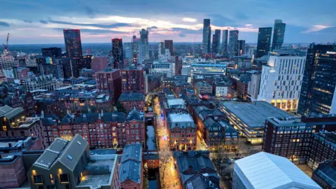 Getty Images Manchester's skyline in the early evening with many modern skycrapers and cranes in the distance and older redbrick buildings in the foreground and at street level