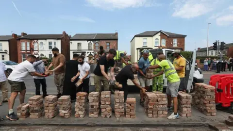 Reuters/Demilade Adelaja Freiwillige bauen nach einer Mahnwache für Opfer von Messerangriffen nach einem gewalttätigen Protest einen Zaun vor der Southport Islamic Community Mosque wieder auf.