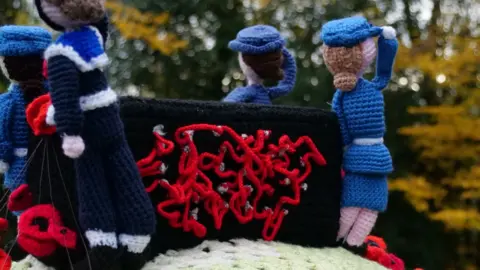 Bletchley Park Trust A knitted WW2 Bombe machine and Women's Royal Naval Service operators in uniform, saluting, seen from behind.
