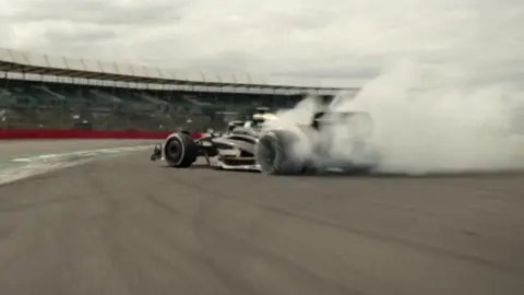 Apple Original Films/Warner Bros A race car on the Silverstone Circuit with smoke coming from the rear tyres