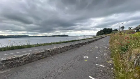 A grey sky, water's edge, and stone road which is The Strand in Portaferry