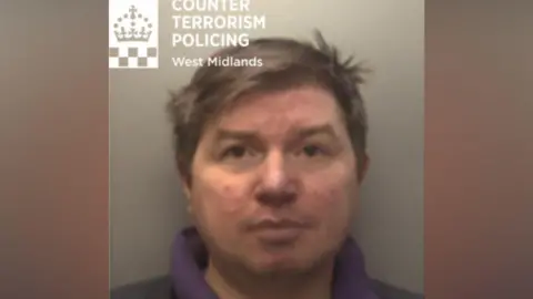 A custody image of Ivan Jennings, a man with short brown hair in a dark coloured outfit with a purple collar visible
