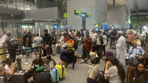 Rob Liddle/BBC People stand and sit in an airport in Doha, Qatar