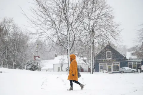 A woman wearing a bright yellow jacket walks through snow in Braemar.