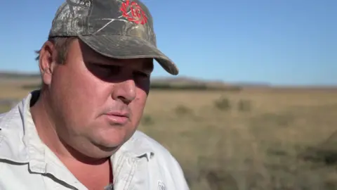 BBC Farmer Roland Collyer is in an open shirt and peak cap which casts a shadow over his eyes.