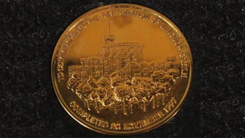 Gold medal with a picture of Windsor Castle and a caption saying "to commemorate the restoration of Windsor Castle completed in 1997"