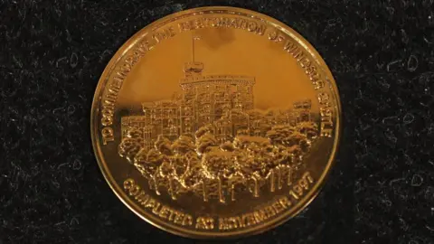 Gold medal with a picture of Windsor Castle and a caption saying "to commemorate the restoration of Windsor Castle completed in 1997"