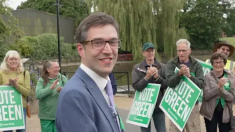 Adrian Ramsay in Diss turning to look over his shoulder with Green Party supporters applauding behind him