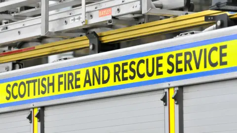 The Scottish Fire and Rescue Service name in black on a gold background on the side of a fire engine