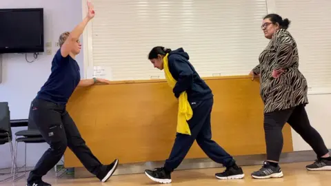 Three woman are wearing fitness clothes and stretching their legs