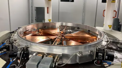 Siemens Healthineers The image shows the cyclotron installed in a clean, controlled indoor environment. It resembles a wheel or rotor.