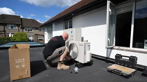 An engineer installs an air conditioning unit on the roof of a residential home. 