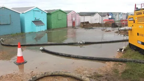 Kevin Boorman A large puddle of sewage with multicoloured beach huts in the background.