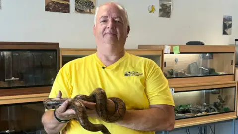 Man dressed in yellow t-shirt holding a Brazilian rainbow boa constrictor in his palms
