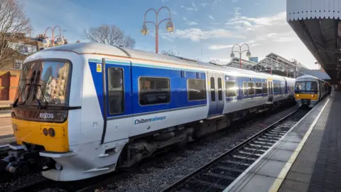 Chiltern Railways A blue-and-white train with Chiltern Railways written on the side at a train station. There is another train in the background by the platform.