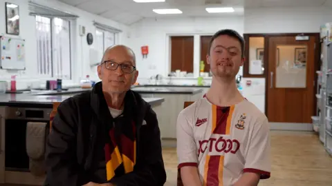 Steve and Matthew Robinson, wearing Bradford City colours with a kitchen behind them