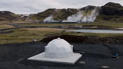 A white dome in the foreground and steam above the carbon capture plant in the distance