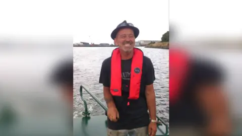 Graham Bennett Graham Bennett smiles at the camera in a picture taken as he is sailing down a river. He is wearing a hat with sunglasses perched on top of it and has a life-preserving aid around his neck.