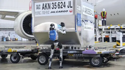 A humanoid robot pushes a cargo container during a media demonstration at Haneda airport in Tokyo on April 27, 2026. Japan Airlines will test the use of such robots at the airport from May, as the airline aims for their practical use in ground handling tasks, such as cargo loading and unloading, in 2028 amid a chronic manpower shortage