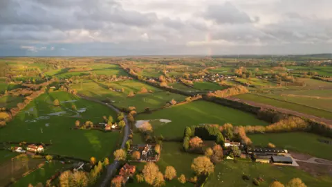 BBC Weather Watchers/Andy The Balloon Man A view from a balloon in the air of countryside with fields of green spread out, dotted with the heads of trees and some houses.