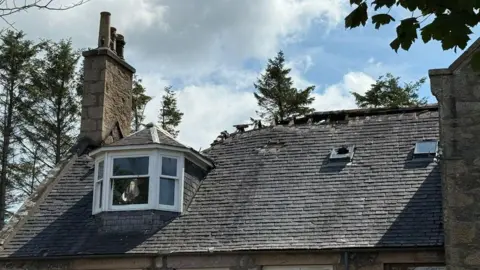 BBC A damaged roof - part of it is clearly missing. A chimney and dormer window remains undamaged. 