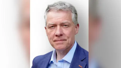 William Clouston William Clouston who has grey hair wears a dark blue jacket and an open necked light blue shirt.