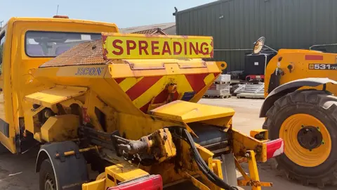 A yellow gritting lorry outside a depot