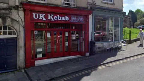 Entrance to UK Kebab, which is a red building near a road.