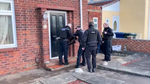 Police atempting to break down a door during a drugs raid as part of Operation Artemis