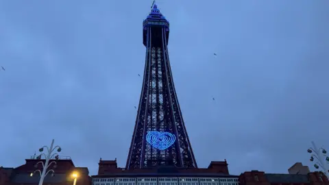 Blackpool tower illuminated blue with a heart shaped neon light installation. 