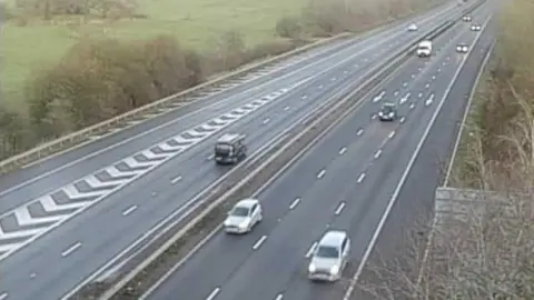 Highways England A traffic camera image of the A1(M) in Hertfordshire. Cars can be seen heading along the motorway with their headlights on during the early morning commute. 