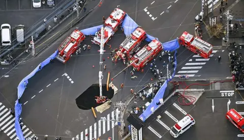 Kyodo via Reuters Sebuah pemandangan udara menunjukkan operasi penyelamatan sedang berlangsung di lubang pembuangan besar yang menelan truk di persimpangan di Yashio, utara Tokyo, Jepang. 28 Januari 2025