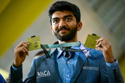 Getty Images Le grand maître médaillé d'or Dommaraju Gukesh montre ses médailles à son arrivée à l'aéroport international de Chennai à Chennai le 24 septembre 2024, après sa victoire à la 45e Olympiade d'échecs FIDE Budapest 2024. (