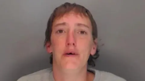 Mugshot of Hewitt. She has short brown hair and appears to be missing her two front teeth.