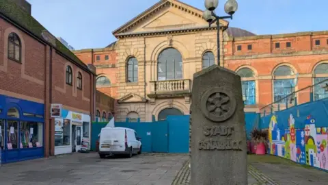 The milestone in front of hoardings in the square