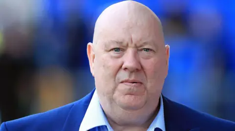 Peter Byrne/Pa Media Joe Anderson memiliki kepala botak dan mengenakan setelan biru dengan kemeja ringan 