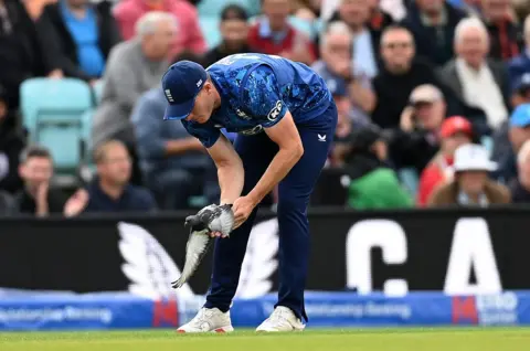 Matthew Potts of England picks up a pigeon on the cricket pitch