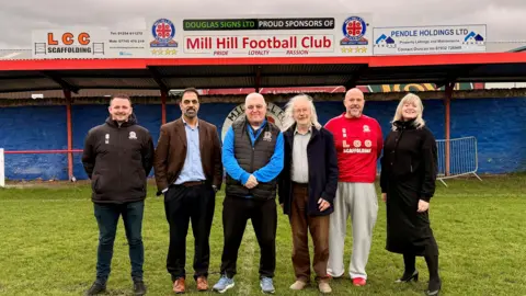 Club and council official pose on the pitch in front of the club's main stand 