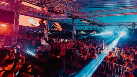 The Hype Factory A crowd of people dancing and watching two DJs play music on stage.