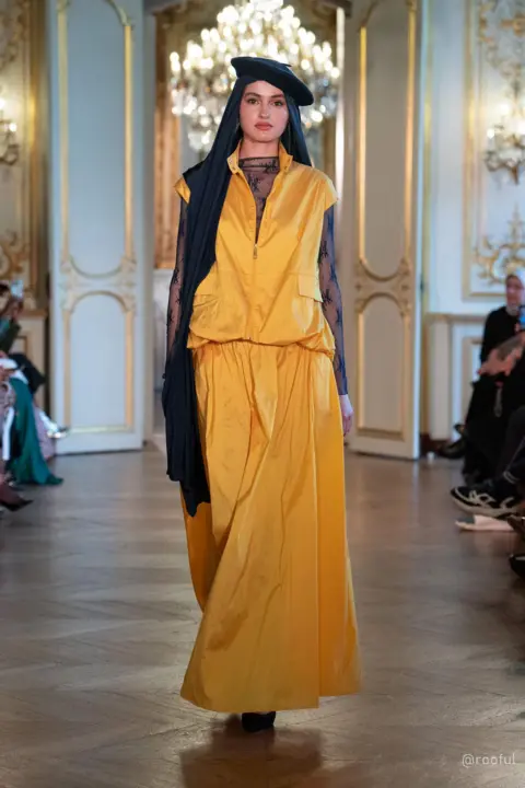Rooful Ali A model wearing a long yellow dress, a blue headscarf and beret