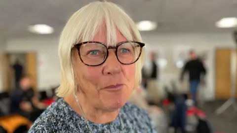 A woman with light hair and leopard print framed glasses.