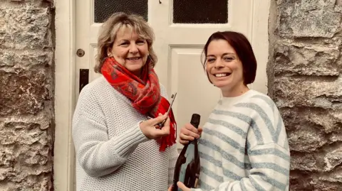 The Crown Inn Emma Lomas standing in front of one of the entrances to The Crown Inn with Karen Clements. Emma is holding a bottle of fizz while Karen is handing her a key to the pub. 