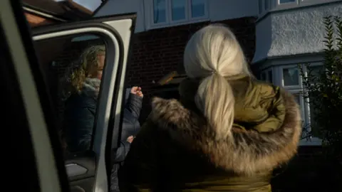 Two women basal   connected  a driveway, their images obscured. Both are wearing heavy   winder padded coats, 1  has shoulder-length curly blonde hairsbreadth  and is looking towards the different   woman, with agelong  blonde hairsbreadth  tied back. The location   tin  beryllium  seen successful  the inheritance  and successful  the foreground is simply a car   door.