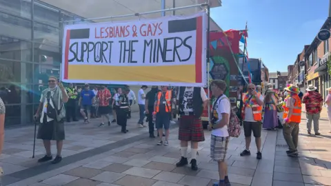 Two people hold a sign which says Lesbian & Gays Support The Miners