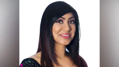 Sharan Sammi/Marta Garcia de Oliveira A smiling Sharan Sammi looks directly at the camera. She has long dark hair and is wearing a black-and-white spotted top. 