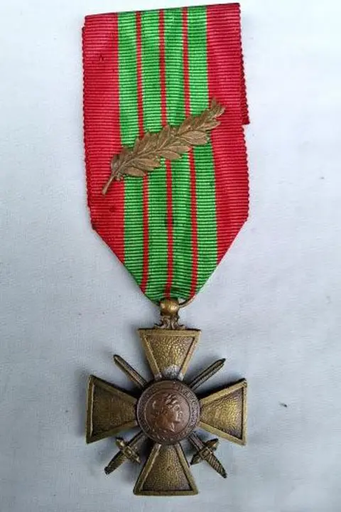 Imperial War Museum A gold medal in the shape of a crucifix with two crossing blades, is attached to a red ribbon with four vertical green stripes