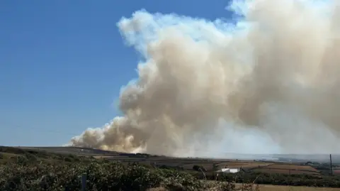 A column of smoke seen against a blue sky.
